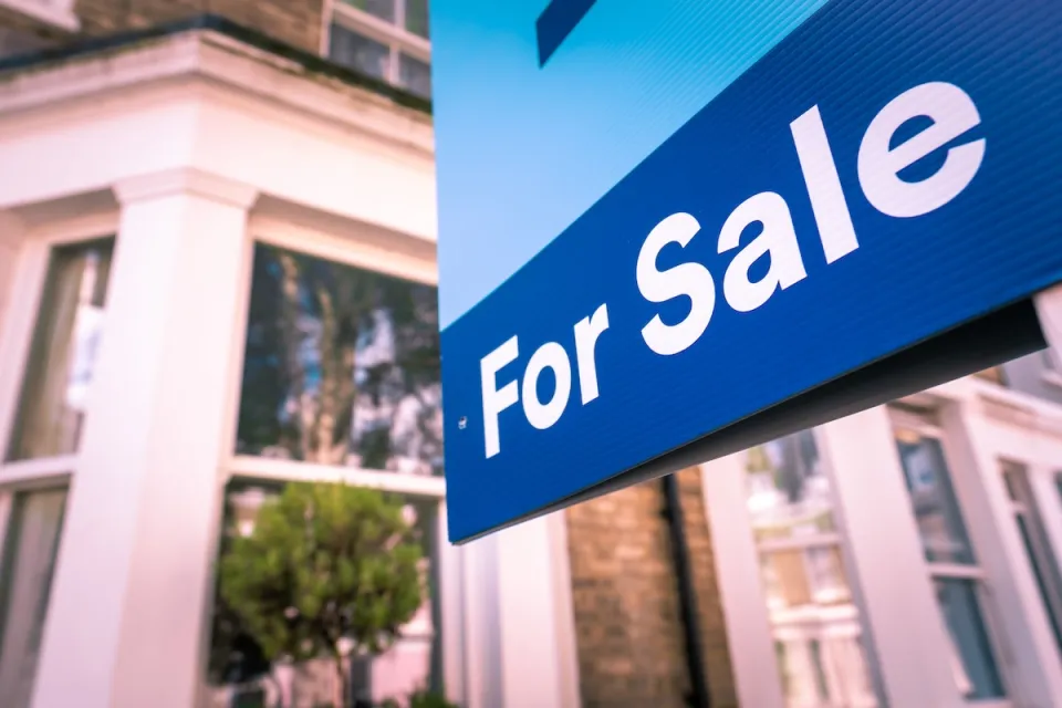 Close-up of blue For Sale sign in front of house.